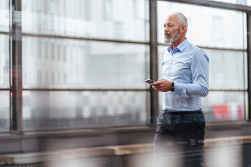 Mature businessman with cell phone at the station platform