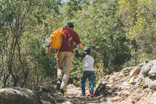 Rear view of tourists school boy and his dad walking a stone footpath in spring forest. Child kid and father wearing casual clothes hiking in summer greenwood leaf forest.
