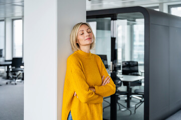 Dreamy woman in a modern office leaning against a wall with closed eyes