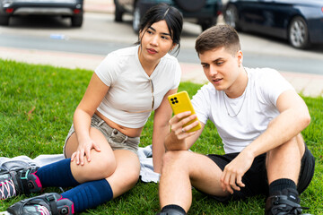Young people using smartphone while resting after inline skating in urban park