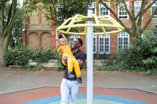 Happy father holding daughter at a climbing frame on a playground