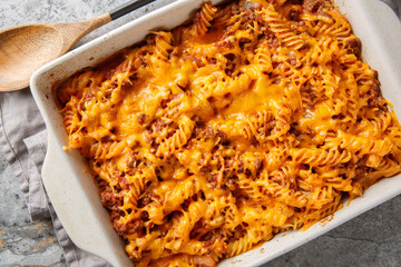Best Sloppy joe casserole is made with ground beef, fusilli pasta, veggies and baked with loads of gooey cheese closeup in the baking dish on the table. Horizontal top view from above