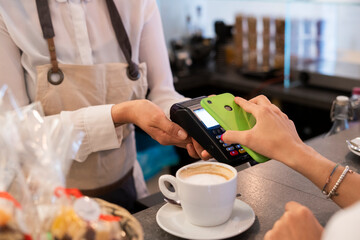 Close-up of customer paying cashless with smartphone in a cafe