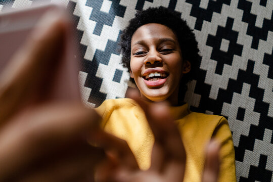 Happy young woman lying on carpet using smartphone