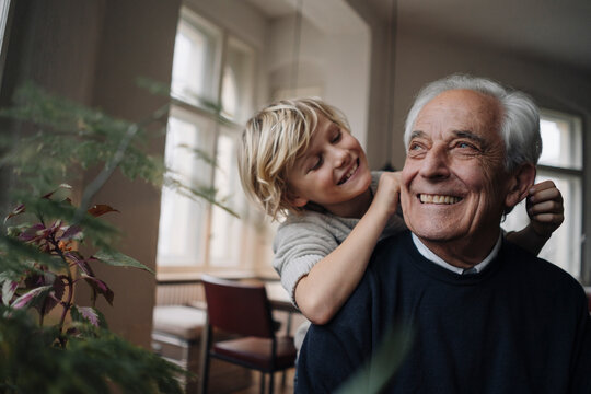 Happy grandson pulling grandfather's ears at home
