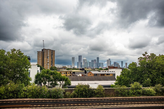 Train tracks leading towards the city's skyline under a dramatic cloudy sky. A mix of residential and commercial high-rises dominate the background.