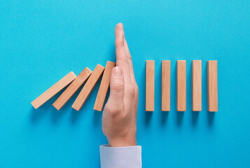 Man stopping wooden blocks from falling on light blue background, top view. Domino effect
