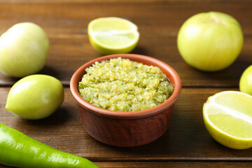 Delicious salsa sauce in bowl and products on wooden table, closeup