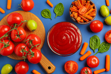 Tasty ketchup and vegetables on blue background, flat lay