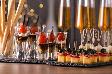 Many different tasty canapes and wine on wooden table against blurred lights