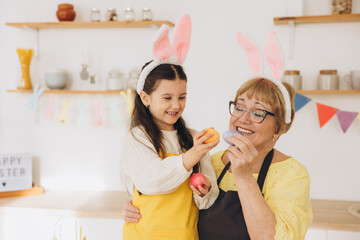 Happy grandmother and granddaughter in easter bunny ears having egg tapping with easter eggs