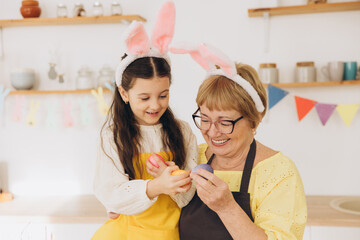 Happy grandmother and granddaughter in easter bunny ears having egg tapping with easter eggs