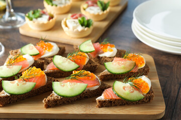 Tasty canapes with salmon and cucumber on wooden table, closeup