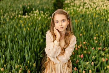 A cute charming girl in a light dress is photographed in a greenhouse with tulip flowers. Women's...