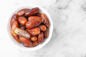 Tasty dried dates in bowl on white marble table, top view. Space for text