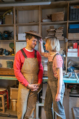 Sweet romantic couple of carpenters playfully try on wooden lampshade as hat in workshop. Family...