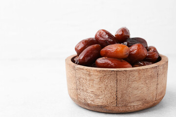Tasty dried dates in wooden bowl on white table, closeup