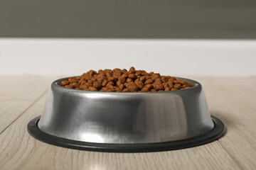 Dry pet food granules in feeding bowl on floor indoors