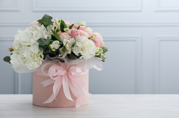 Beautiful bouquet in box on white wooden table against light wall. Space for text