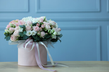 Gift box with bouquet of beautiful flowers and eucalyptus branches on wooden table against light blue wall. Space for text