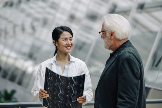 Smiling female doctor with x-ray and senior man talking - Powered by Adobe