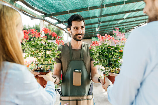 Smiling worker in a garden center showing plants to customers