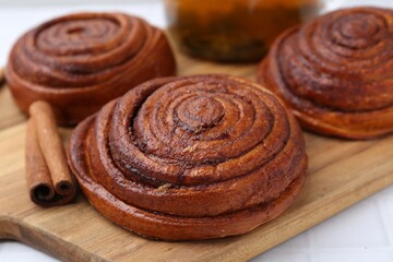 Delicious cinnamon rolls and stick on white tiled table, closeup
