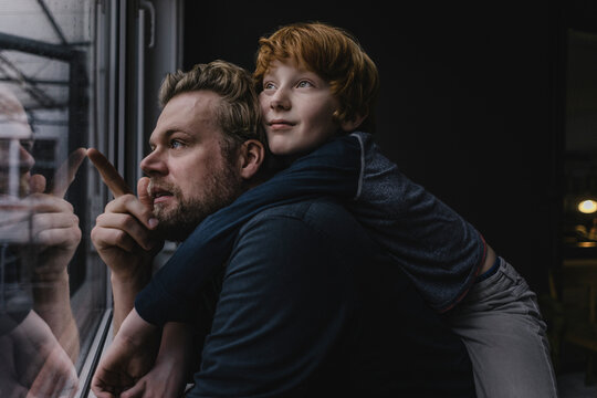 Father and son looking together out of window on rainy day