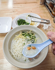 Congee with noodles, chives, ginger, and a spoon tasting a bite.