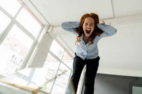 Portrait of redheaded woman standing on desk in a loft freaking out