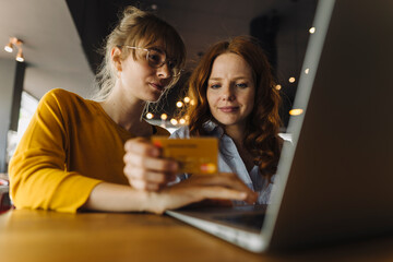 Two female friends with laptop and credit card in a cafe