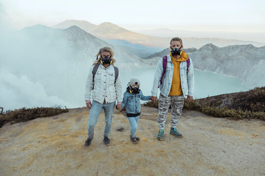 Family with respirator masks standing hand in hand at the edge of volcano Ijen, Java, Indonesia