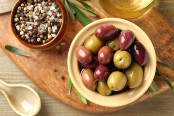 Tasty olives in bowl, leaves and spices on wooden table, flat lay