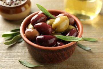 Tasty olives and leaves in bowl on wooden table, closeup