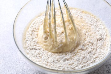 Whisk and bowl of dough on grey table, closeup