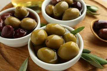 Delicious marinated olives in bowls and green leaves on table, closeup
