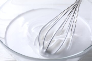 Whisk and whipped cream in bowl on table, closeup