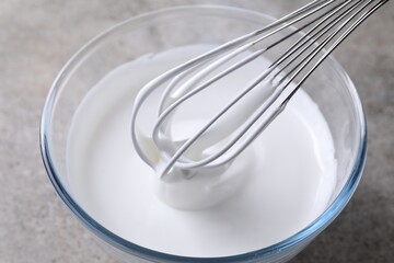 Whisking whipped cream in bowl on grey table, closeup