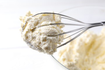 Bowl with whisk and whipped cream on white table, closeup