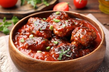 Delicious meatballs with tomato sauce and herbs on wooden table, closeup