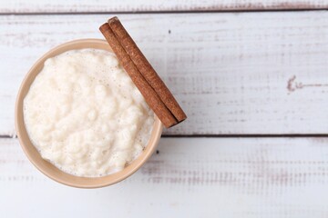 Tasty rice pudding with cinnamon on white wooden table, top view. Space for text