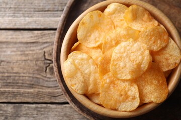 Tasty potato chips in bowl on wooden table, top view. Space for text
