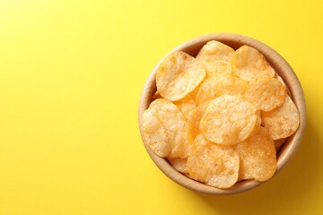 Tasty potato chips in bowl on yellow background, top view. Space for text