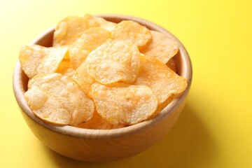 Tasty potato chips in bowl on yellow background, closeup