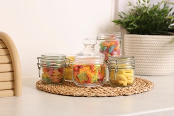 Tasty gummy candies in glass jars on white table