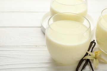 Delicious vanilla milk in glasses, pods and flower on white wooden table, closeup. Space for text