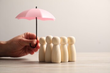 Woman holding umbrella over human figures at light wooden table, closeup. Insurance concept