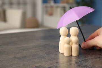 Insurance concept. Woman holding umbrella over human figures at grey table indoors, closeup. Space...