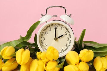 Spring time. Alarm clock and beautiful tulips against pink background, closeup