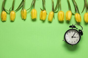 Spring time. Alarm clock and beautiful tulips on green background, flat lay. Space for text